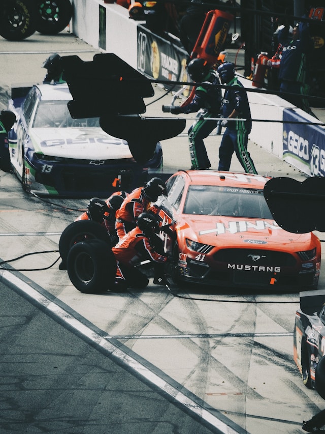 samochód wyścigowy stoi w pit stopie, mechanicy go naprawiają